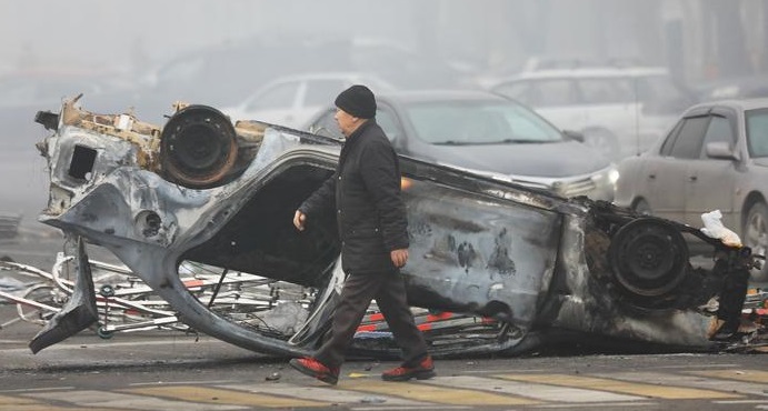 阿拉木圖一名男子經過因抗議而被燒毀的汽車。.jpg 阿拉木圖一名男子經過因抗議而被燒毀的汽車。.jpg